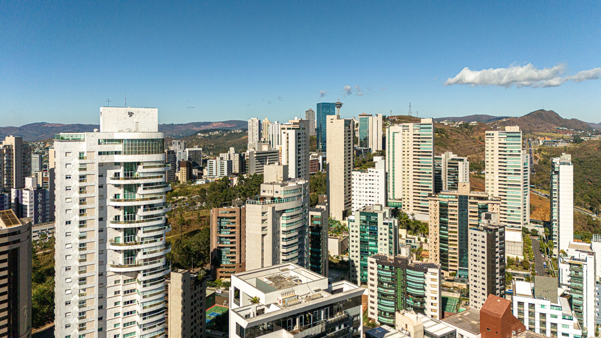 Aerial view down Avenida Afonso Pena in downtown Belo Horizonte, featuring mid-century towers, a vibrant mural, and the Serra do Curral ridge.