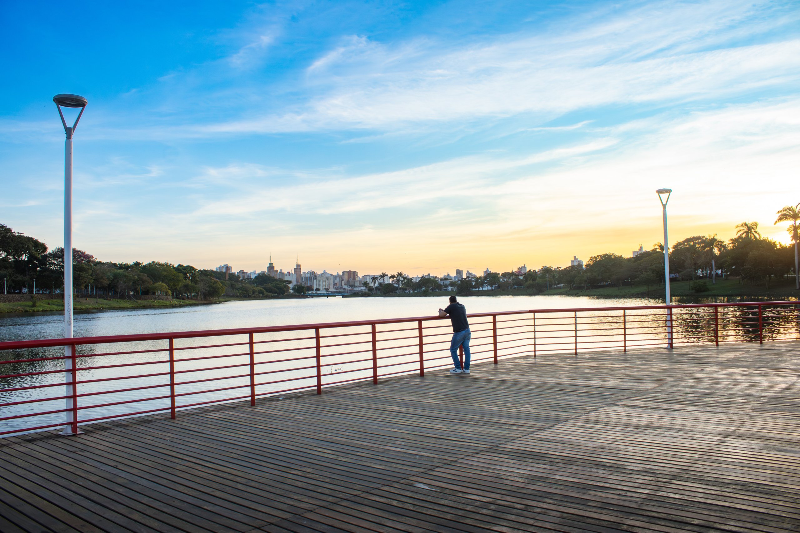 Sรฃo Josรฉ do Rio Preto โ pedestrian deck over Represa lake at sunset with single visitor and distant skyline.